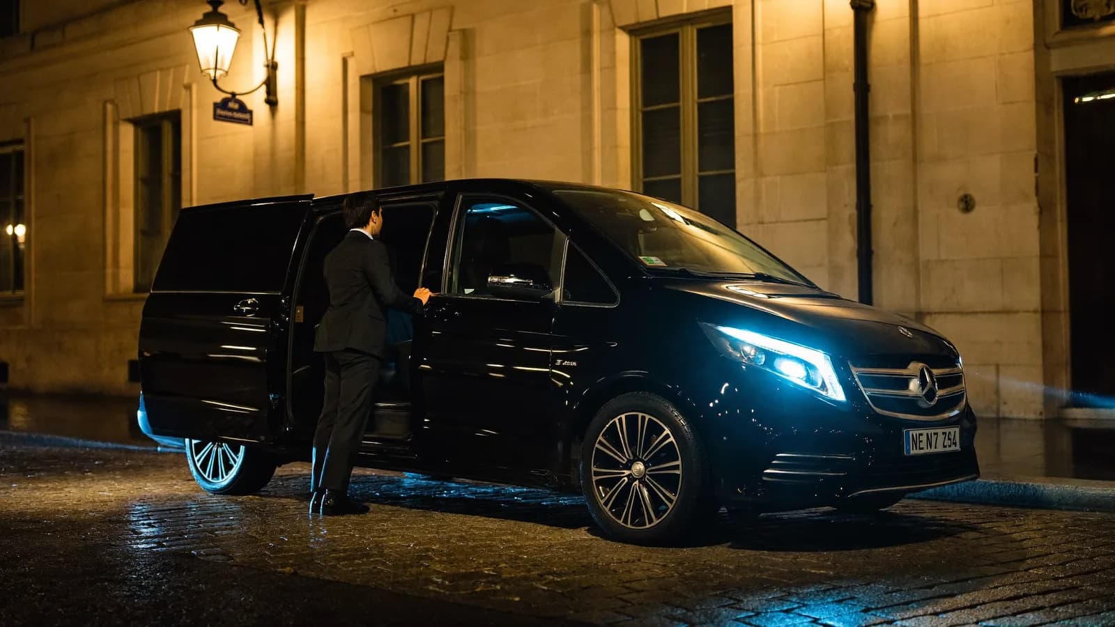 Chauffeur opening the rear door of a black Mercedes V-Class in Paris at night