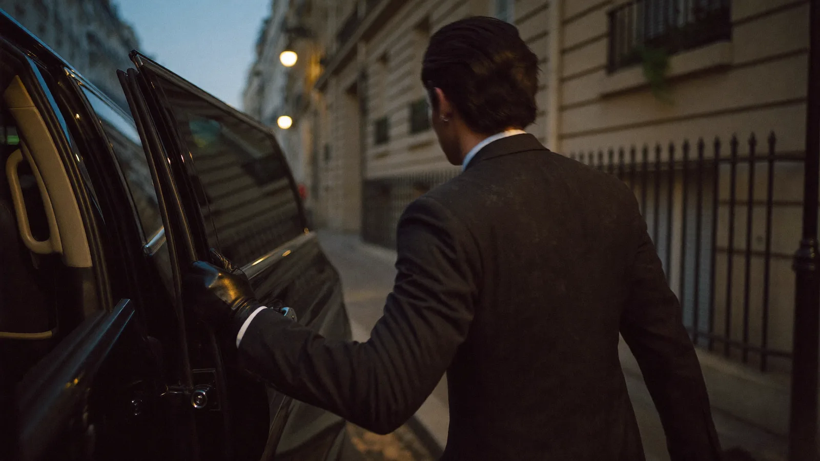 Chauffeur in a dark suit holding the rear door of a business van in Paris
